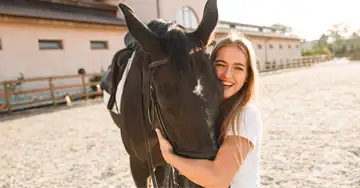 eine junge Frau umarmt den Kopf ihres braunen Pferdes